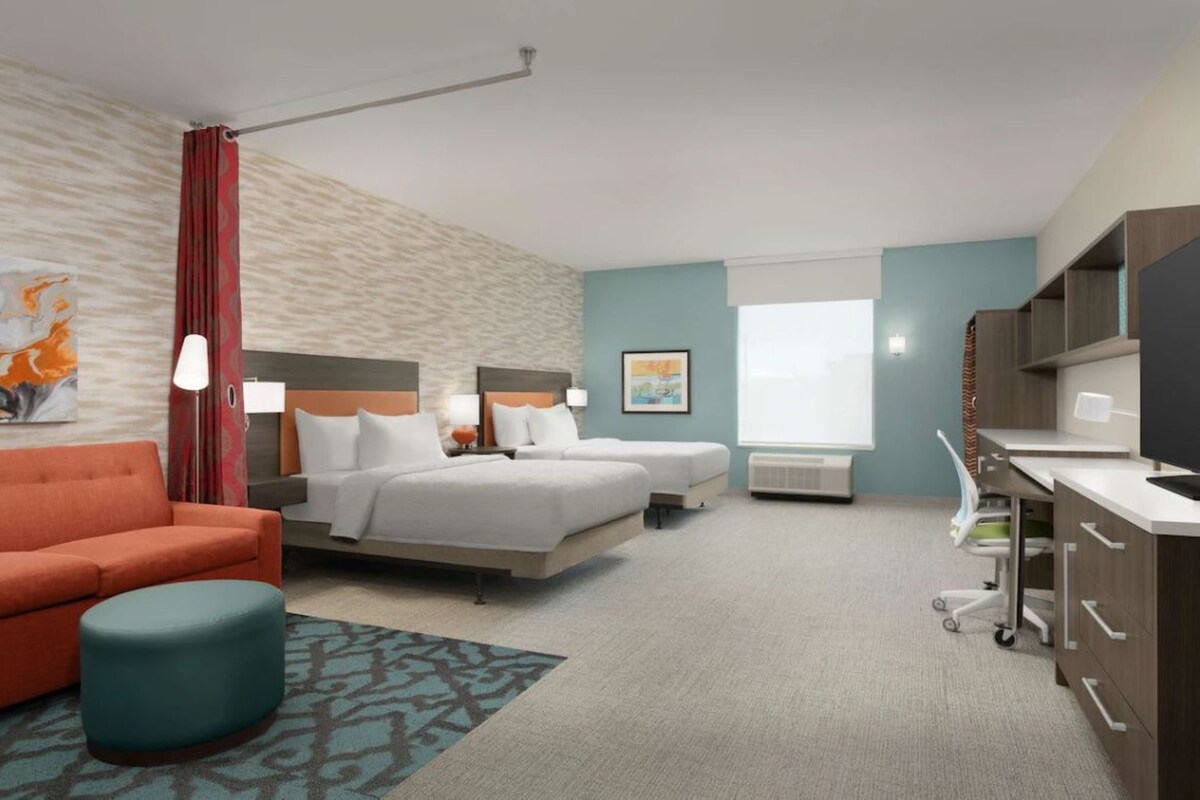 A hotel room with a bed, two bedside tables, a desk, a chair, a sofa, a TV, and a window.