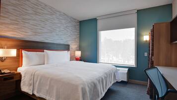 Une chambre d’hôtel comprenant un lit, une table de chevet, une lampe, un bureau, une chaise et une grande fenêtre.