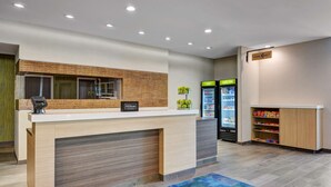 A hotel reception area with a wooden reception desk, a minibar, and a vending machine. - Home2 Suites by Hilton Fort Mill, SC (Fort Mill)