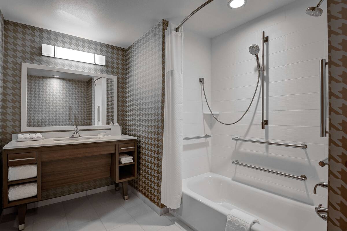 Une salle de bain moderne équipée d’une douche, d’un lavabo avec un miroir et d’un meuble-lavabo avec des serviettes.