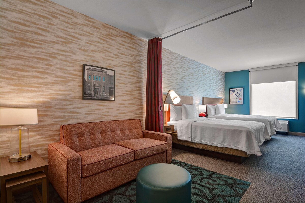 A hotel room with a sofa, a bed, a nightstand, a lamp, and a framed picture on the wall.