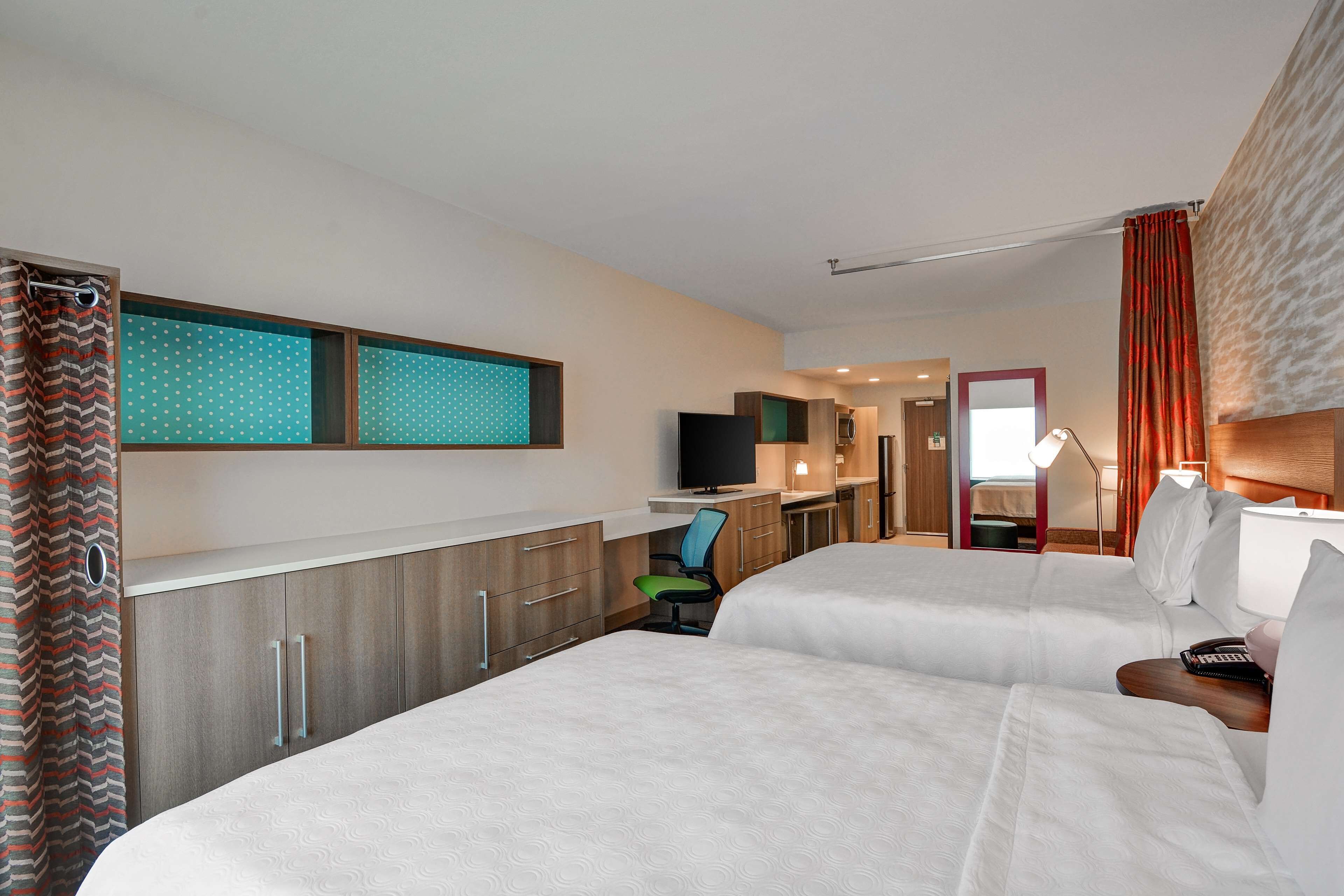 A hotel room with two beds, a desk, a TV, and a bathroom visible through an open door.