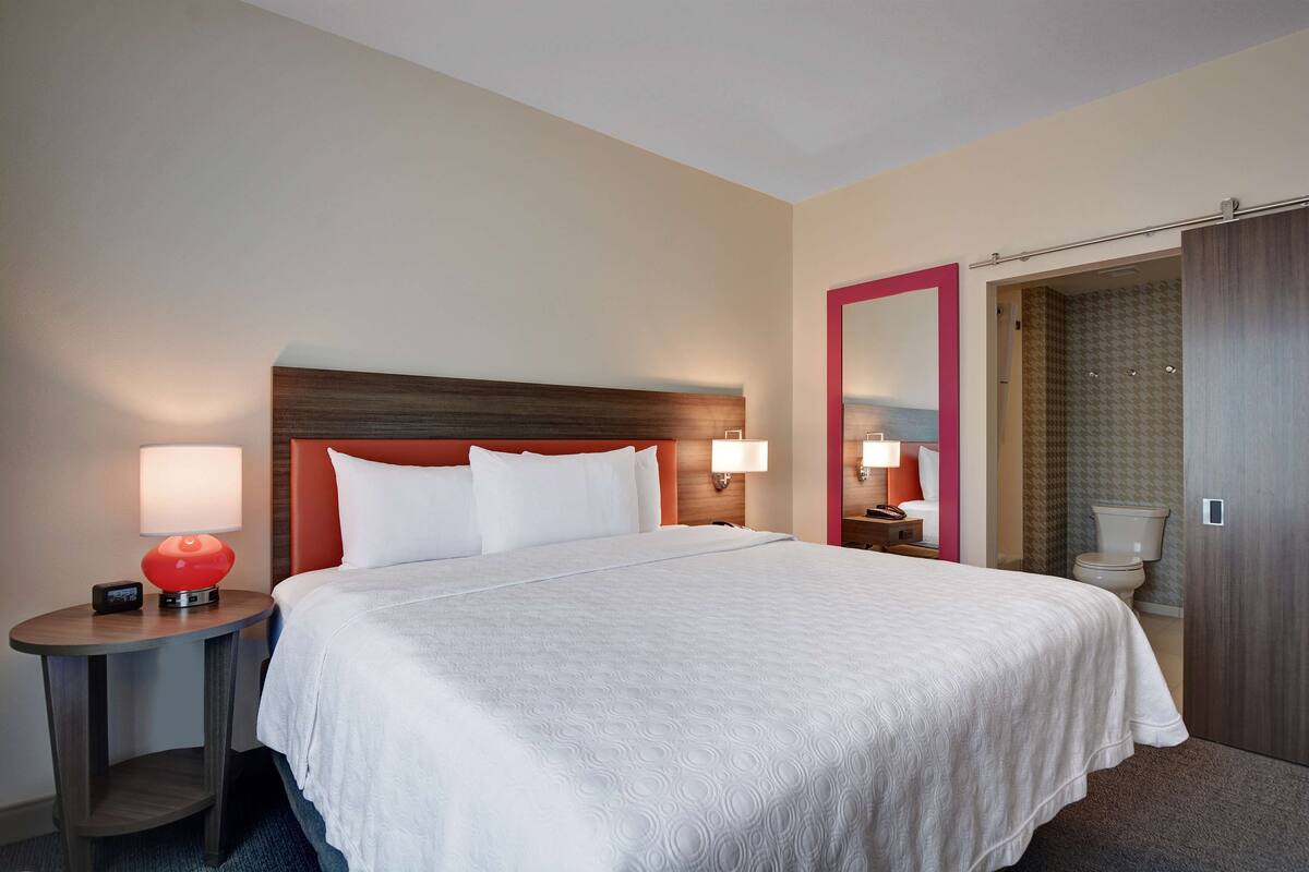 Une chambre d’hôtel avec un grand lit, une table de chevet avec une lampe, une commode, un miroir et une armoire.