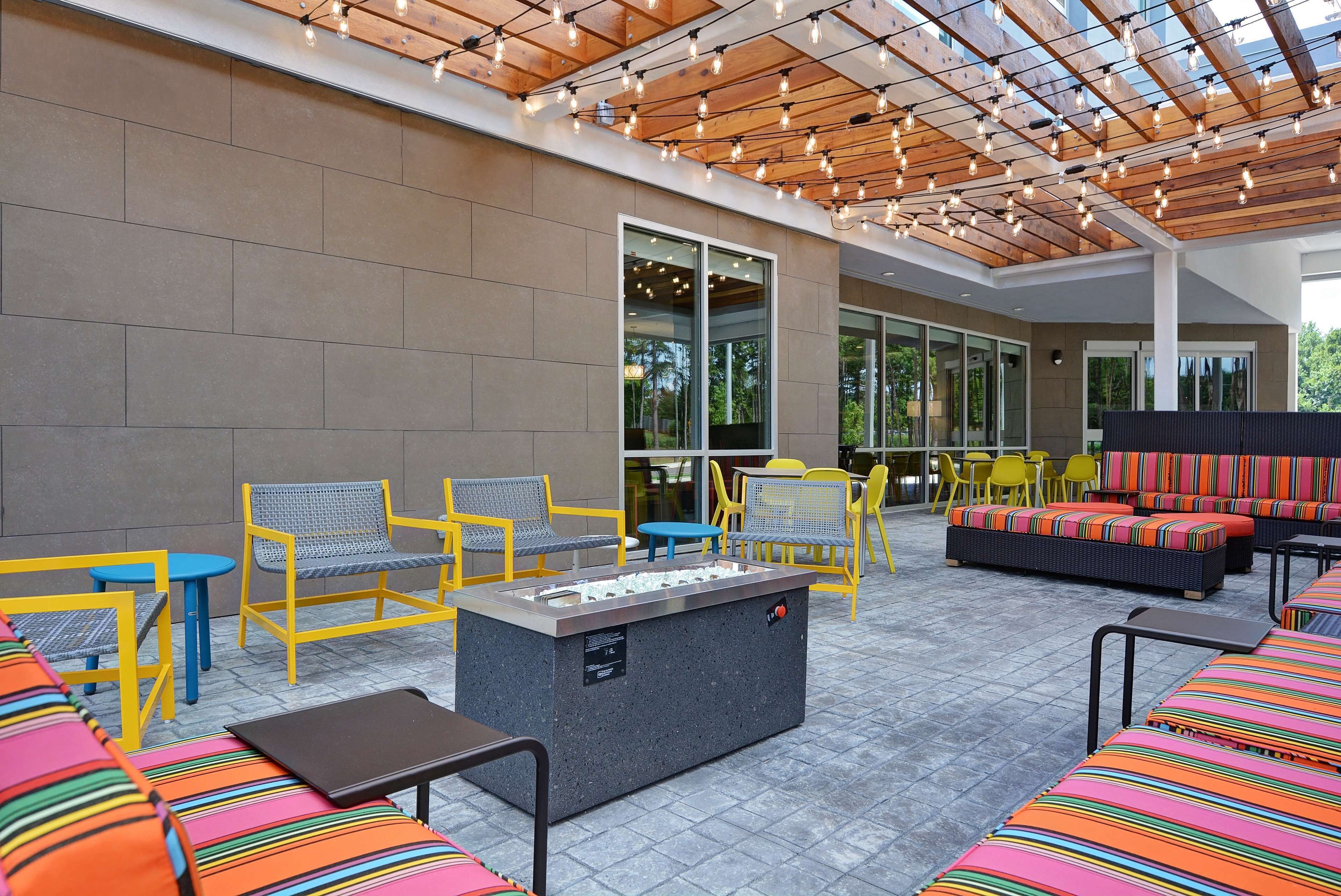 An outdoor seating area with yellow and gray chairs, a fire pit, and a modern building with large windows in the background.