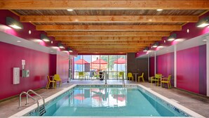 An indoor swimming pool with wooden beams, bright pink walls, and yellow chairs. - Home2 Suites by Hilton Fort Mill, SC (Fort Mill)