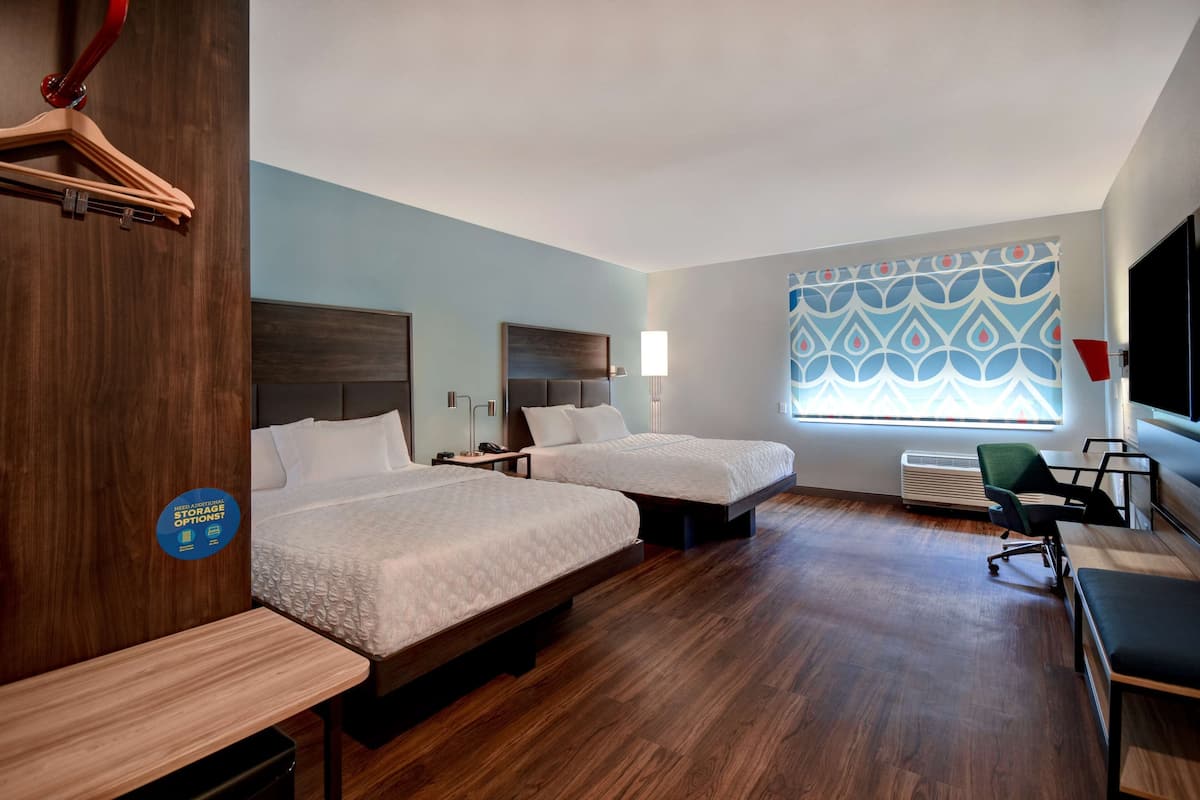 A hotel room with two beds, a desk, a chair, and a TV.