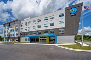 Un edificio moderno de hotel con un llamativo letrero de 'tru by Hilton', ventanas grandes y una zona de entrada cubierta.