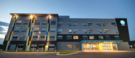 A modern hotel building with a flat roof, multiple floors, and a well-lit entrance.