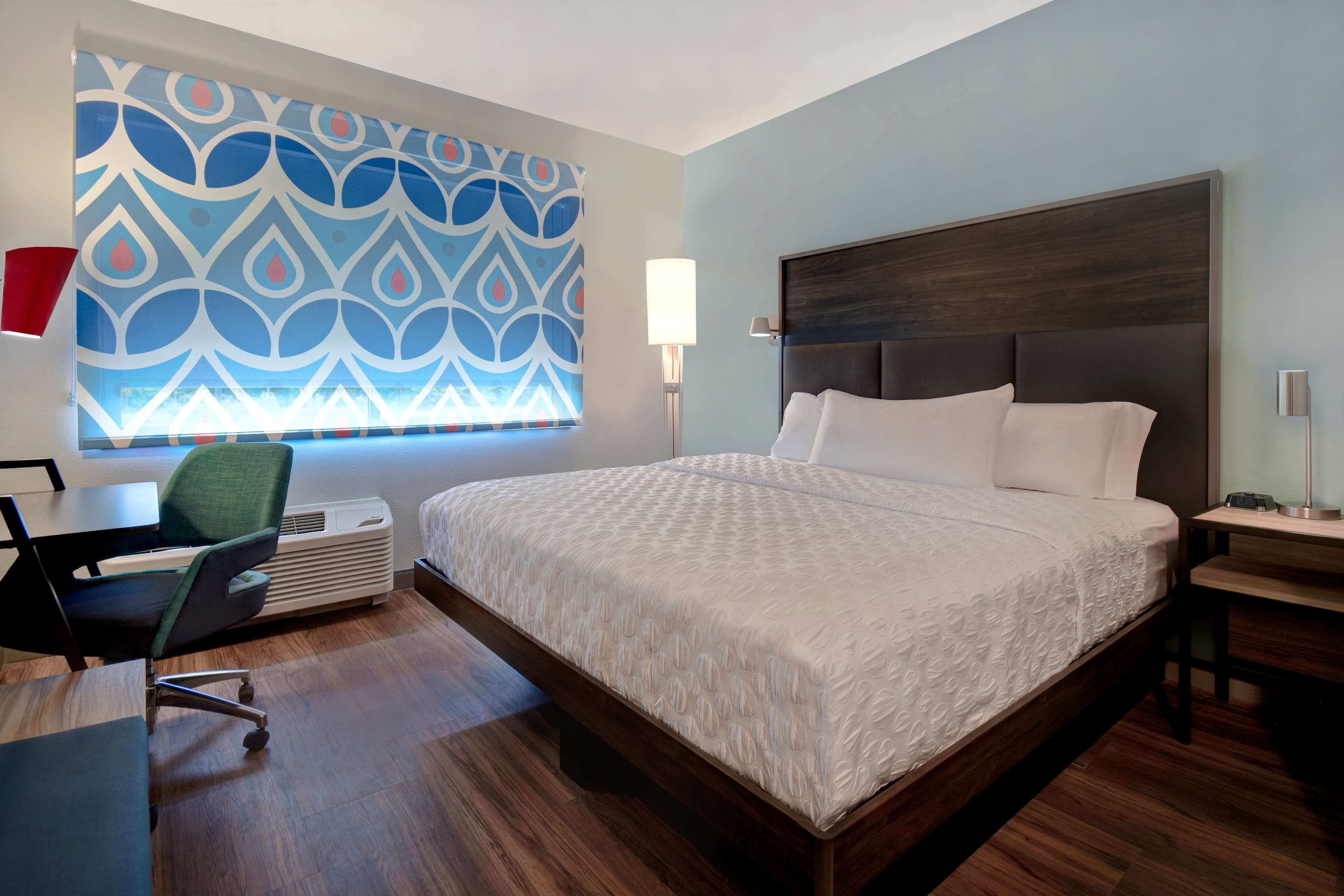 A modern hotel room with a large bed, a desk with a chair, and a patterned wall.