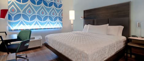 A modern hotel room with a large bed, a desk with a chair, and a patterned wall.