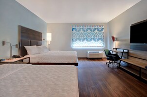 Habitación de hotel con dos camas, un escritorio, una silla, un televisor y una ventana con cortinas estampadas.