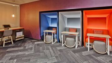 A hotel room with a desk, two seating areas with tables and chairs, and a patterned carpet.