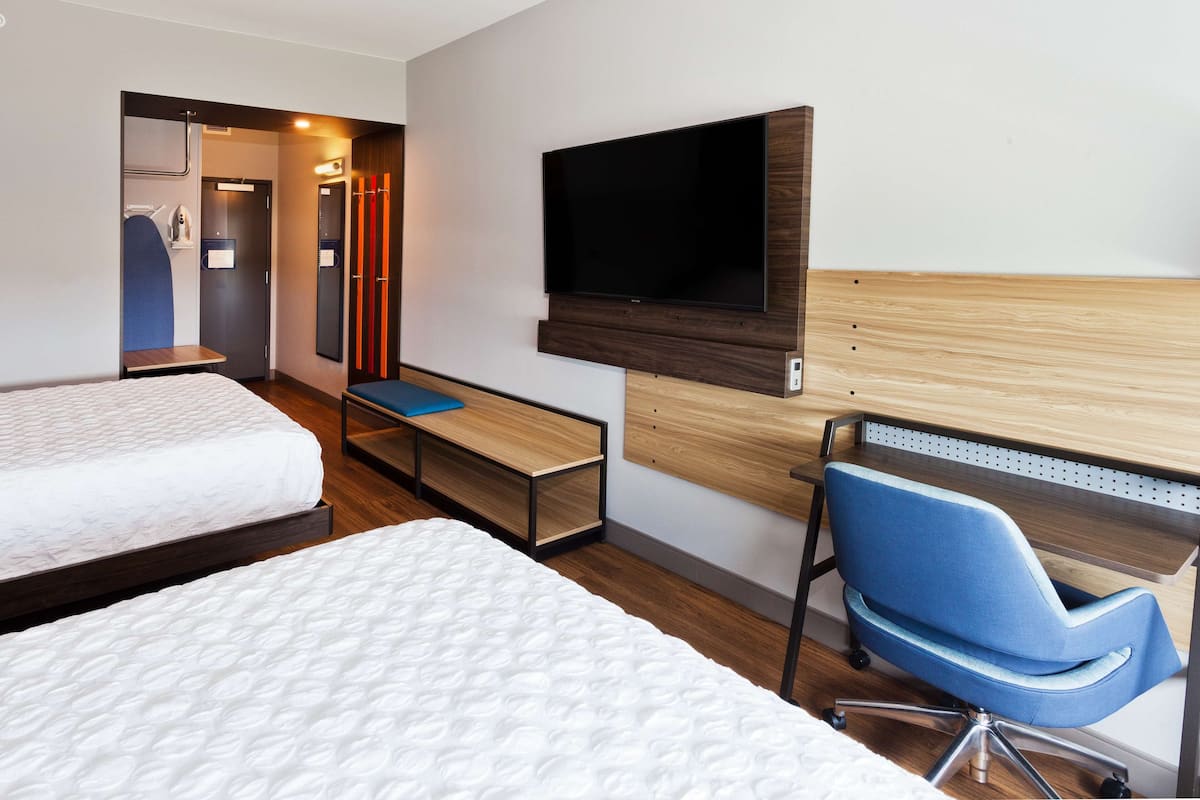 Ein Hotelzimmer mit zwei Betten, einem Schreibtisch, einem Stuhl, einem Fernseher und einem Kleiderschrank.