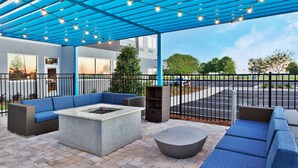 An outdoor patio area with blue seating, a fire pit, and a covered space with string lights. - Tru By Hilton Prattville (Prattville)