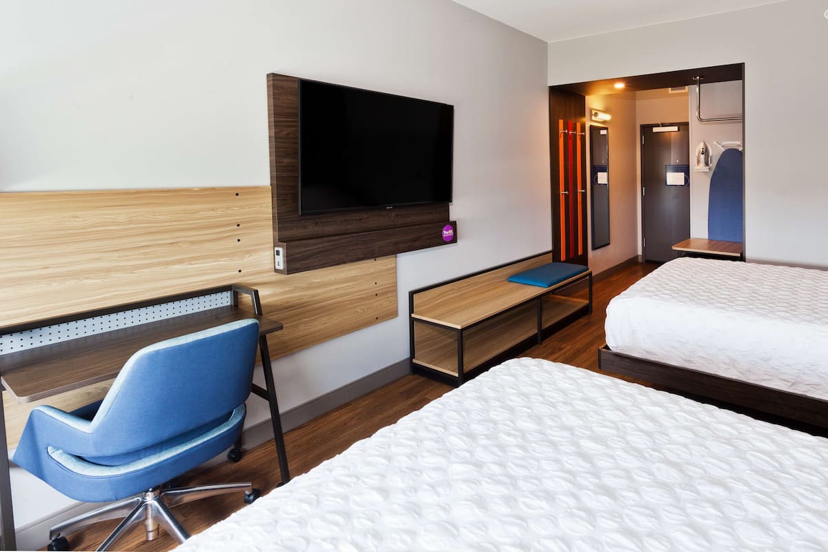 Ein Hotelzimmer mit einem Bett, einem Schreibtisch mit Stuhl, einem an der Wand montierten Fernseher und einem Kleiderschrank.