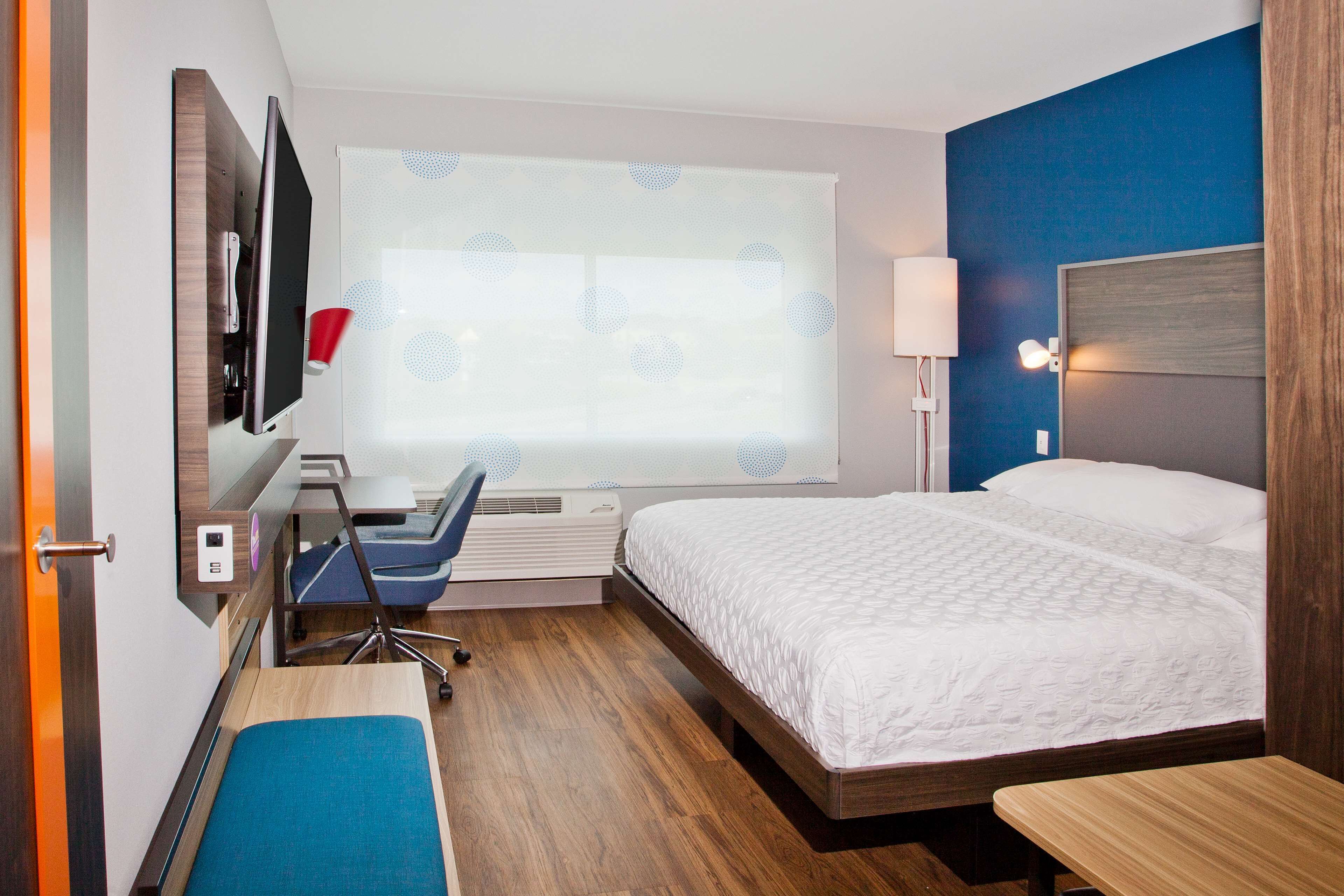 A hotel room with a bed, desk, chair, and a large window with a view.