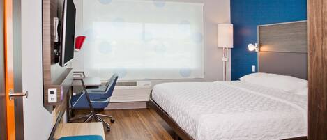 A hotel room with a bed, desk, chair, and a large window with a view.