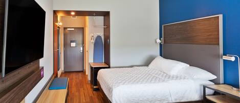 Una habitación de hotel con una cama, un televisor, un banco y un escritorio.