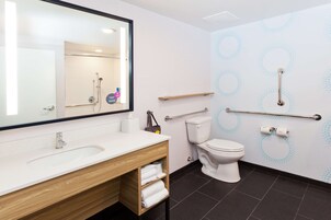 Un baño moderno con lavamanos, espejo, inodoro y barras de apoyo.