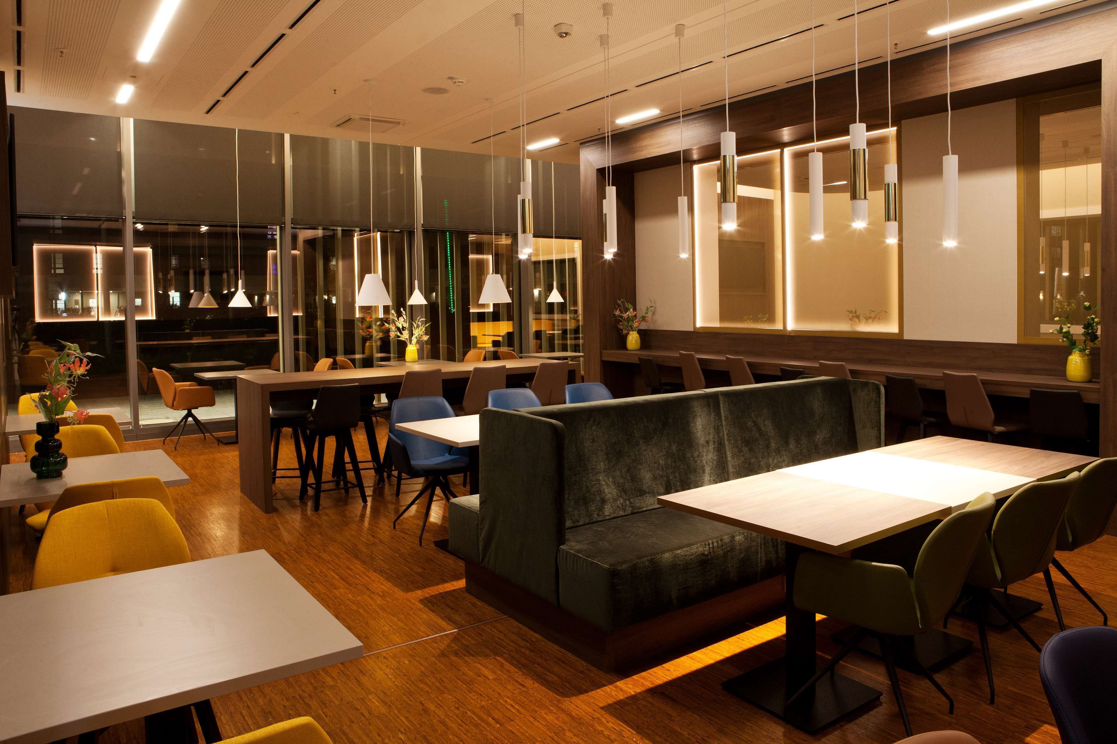 A modern restaurant with wooden flooring, green upholstered booths, and white tables.