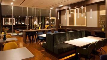 A modern restaurant with wooden flooring, green upholstered booths, and white tables.