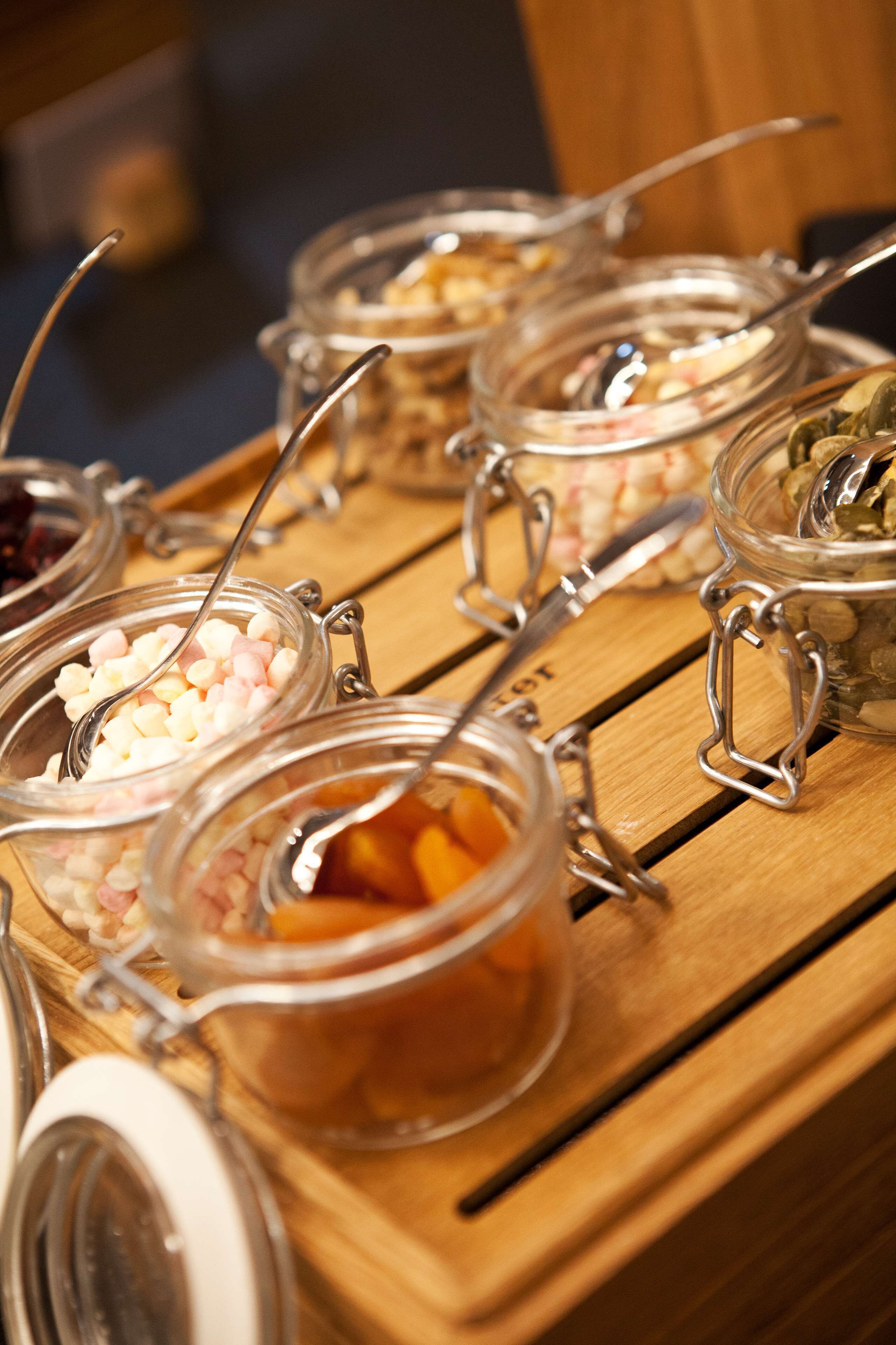 Una mesa buffet de madera con frascos de vidrio que contienen diferentes alimentos.