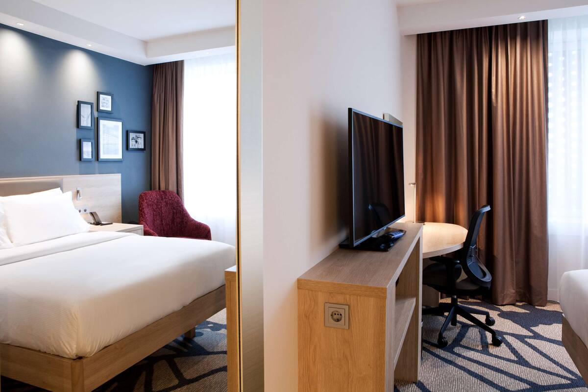 Una habitación de hotel con cama, escritorio con computadora, televisor y silla.