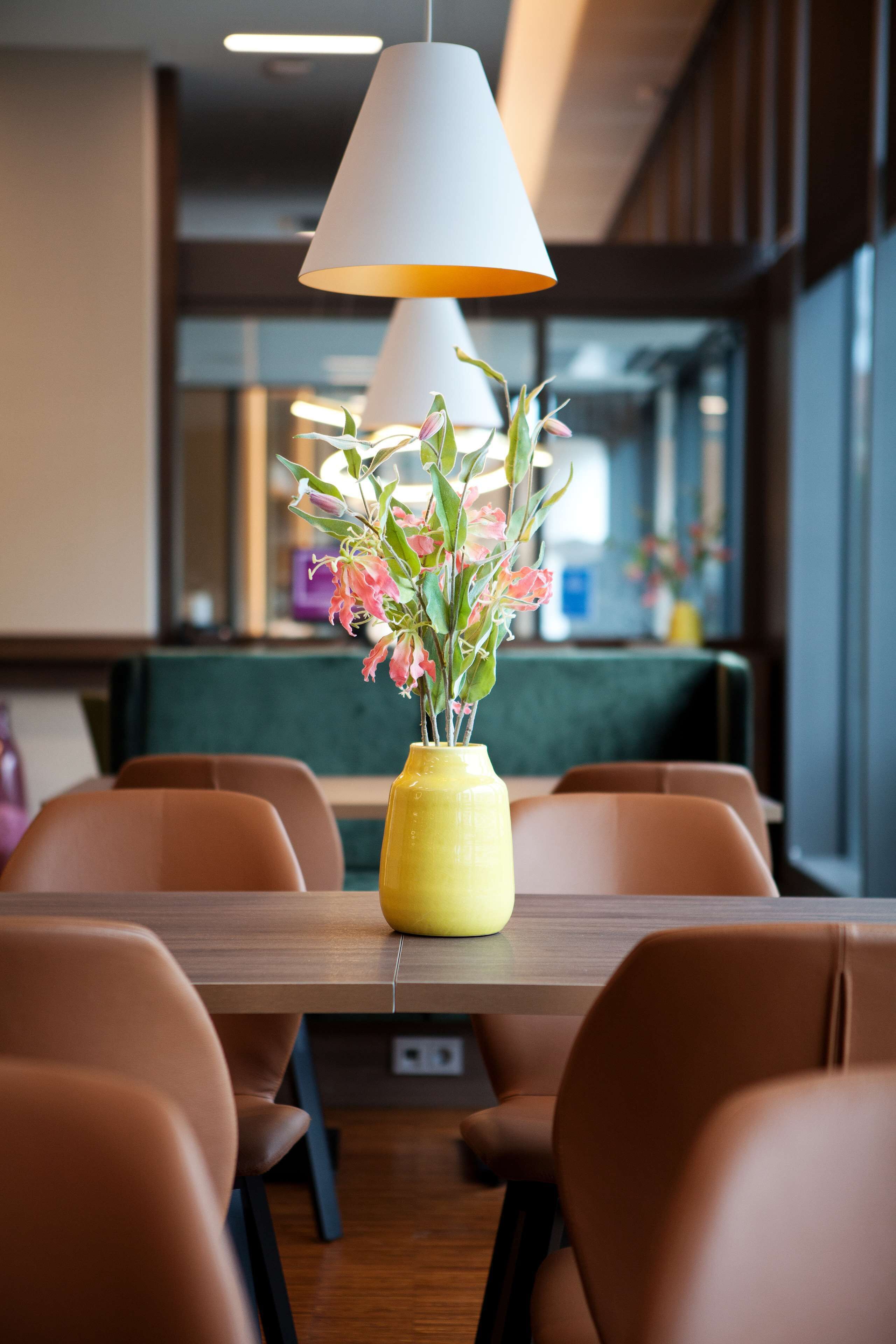 A dining area with a wooden table, brown chairs, a yellow vase with flowers, and pendant lighting.