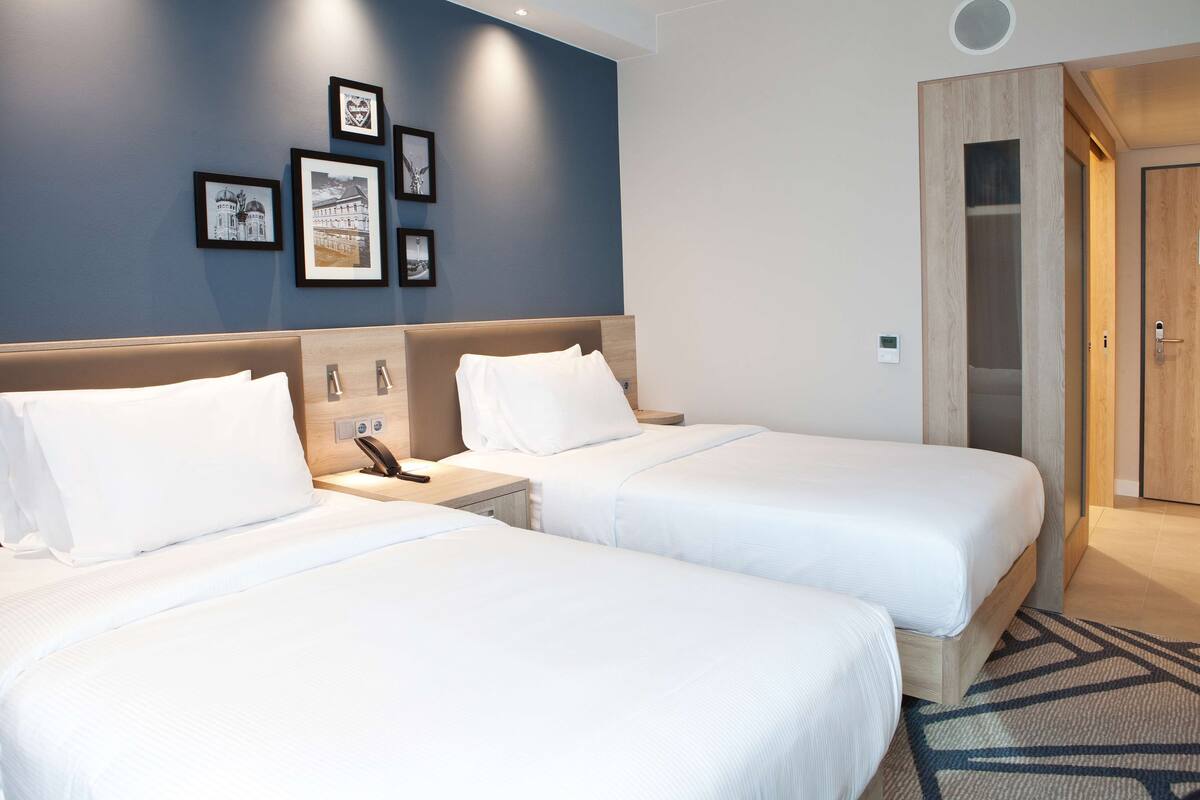 Habitación de hotel con dos camas, una mesita de noche, teléfono en la pared y cuadros enmarcados.