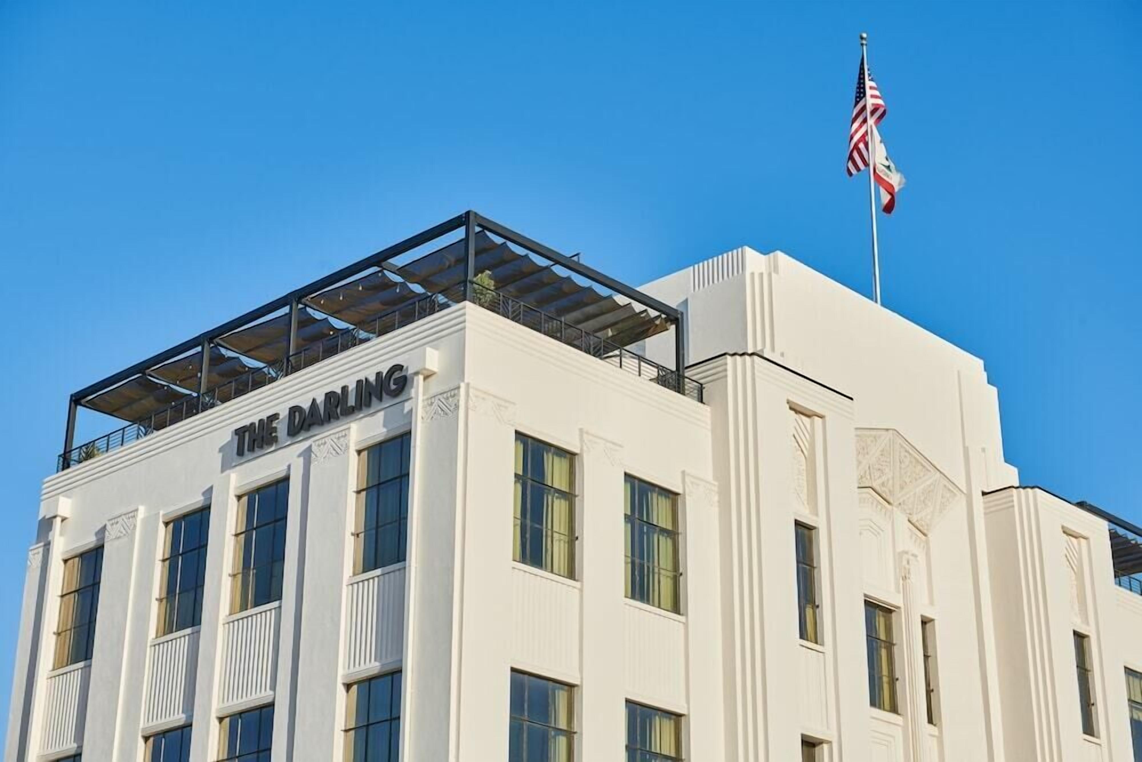 A building with the sign "THE DARLING" on the facade, featuring a balcony with a metal railing and an American flag on top.