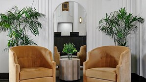 A lobby with two armchairs, a round table with a vase, and large potted plants.