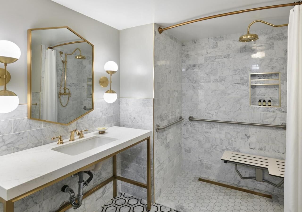 Een moderne badkamer met een witte wastafel, gouden details, een douche met een gouden douchekop en een douchecabine betegeld met marmer.