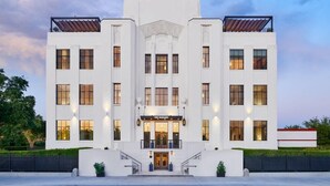 A white, multi-story building with a central entrance, large windows, and a flag at the top.