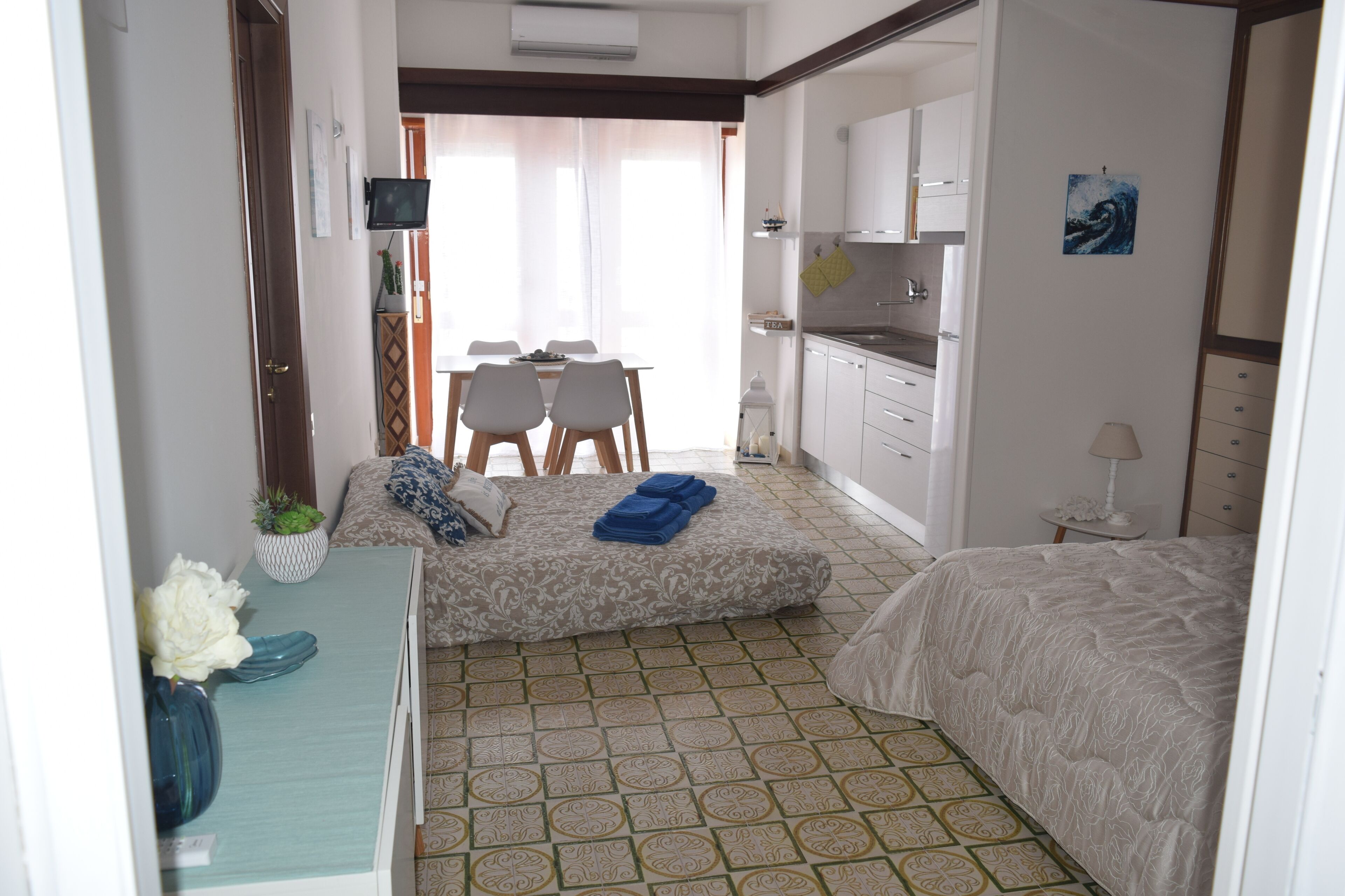 A compact hotel room with a bed, a small desk, a dining table with chairs, a kitchenette, and a bathroom.