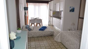 A compact hotel room with a bed, a small desk, a dining table with chairs, a kitchenette, and a bathroom.