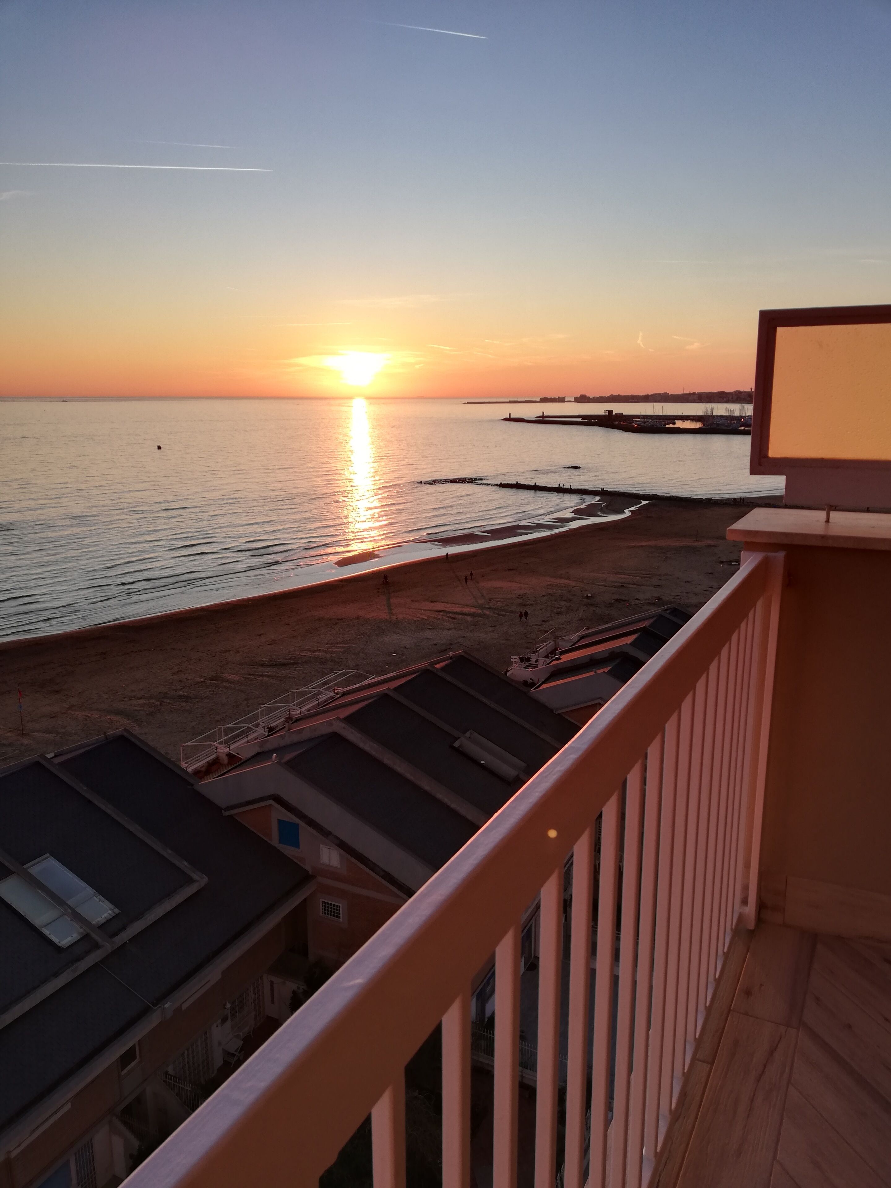 A sunset view from a balcony overlooking a beach with a pier in the distance.