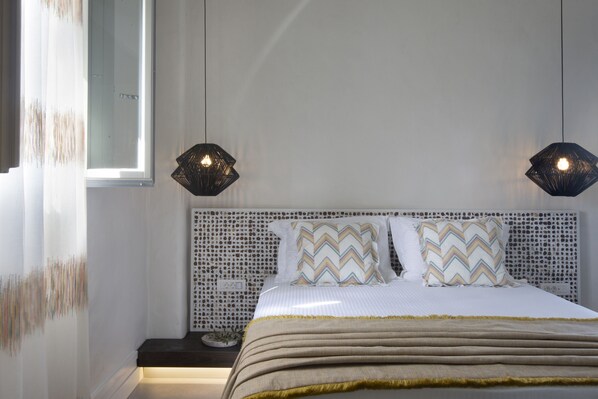 A neatly made bed with patterned pillows, a bedside table with a lamp, and a wall with a textured pattern. - Parion Opus - Adults Only (Paros)