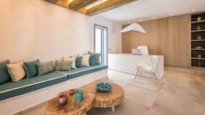 A modern living room with a wooden ceiling, a sofa with patterned cushions, a round coffee table, and a white reception desk. - Parion Opus - Adults Only (Paros)