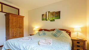 A bedroom with a bed, two bedside tables, a wooden wardrobe, and three wall-mounted paintings.