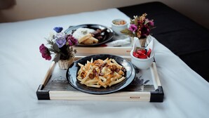 A tray with a plate of fries and bacon, a bowl of sauce, and a small vase with flowers on a bed. - Paris Hotel by H Hotéis Business (Taguatinga)