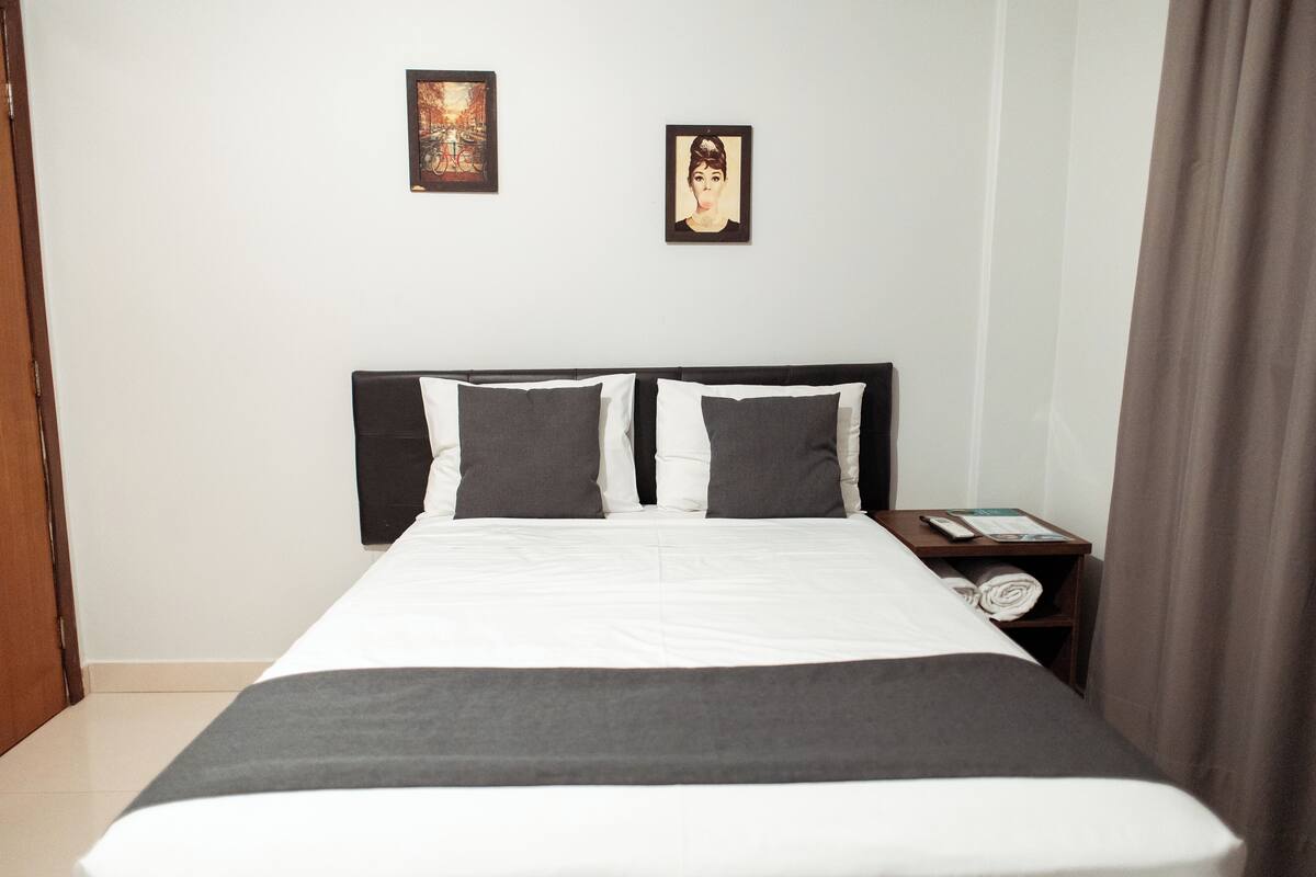 A neatly made bed with a white and gray bedspread, two pillows, and a wooden headboard. There are two framed pictures on the wall above the bed.
