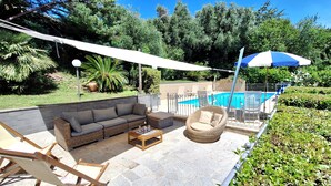 En udendørs patio med pool, siddepladser og en pergola der giver skygge.