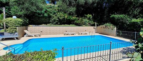 Une piscine rectangulaire, dotée d’une plage carrelée et entourée d’une clôture en métal.