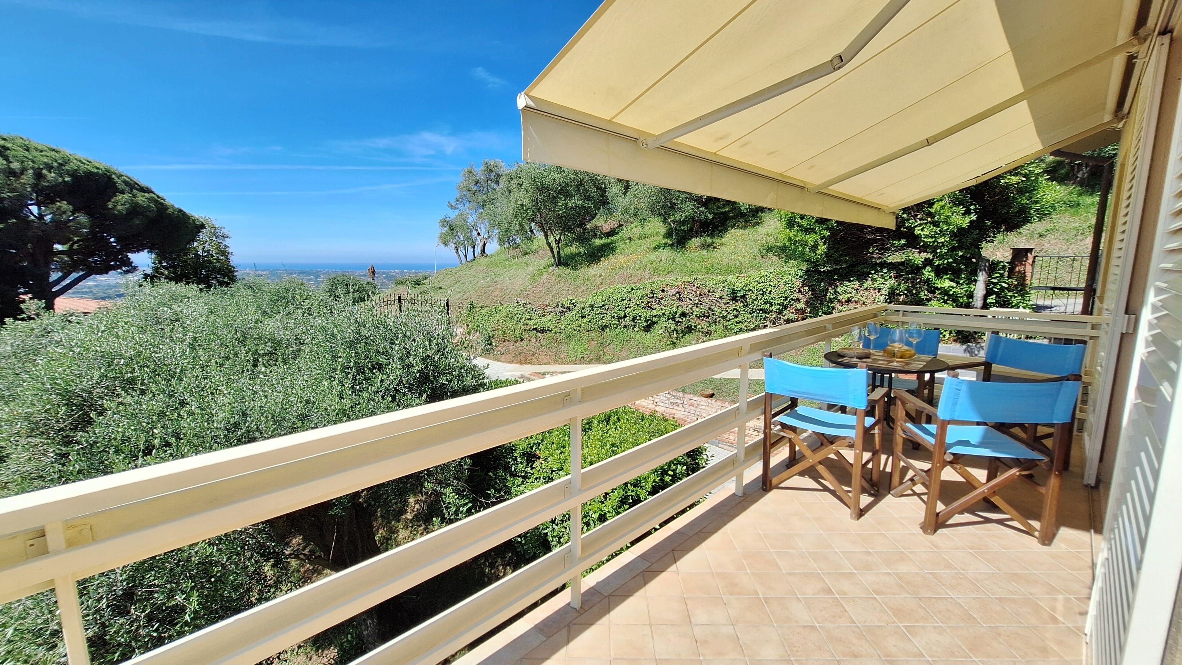 Un balcon avec une table et des chaises, offrant une vue sur un paysage luxuriant et la mer.