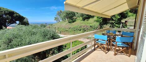 Un balcon avec une table et des chaises, offrant une vue sur un paysage luxuriant et la mer.