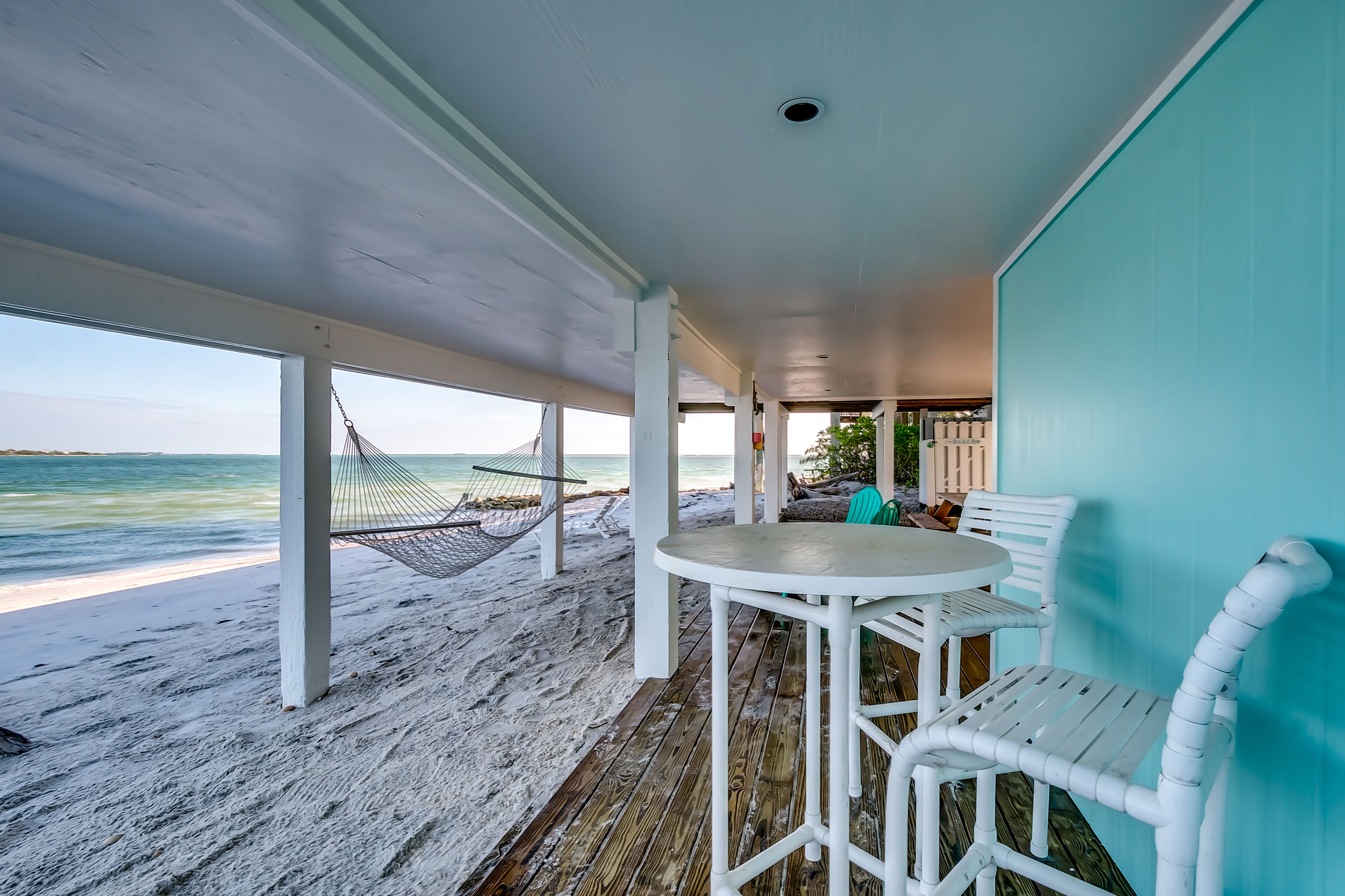 A beachside patio with a white table and chairs, a hammock, and a view of the ocean.