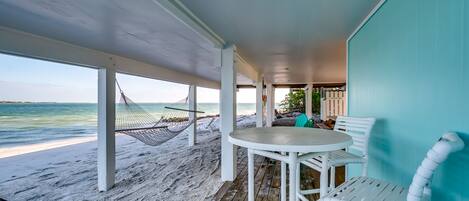 A beachside patio with a white table and chairs, a hammock, and a view of the ocean.