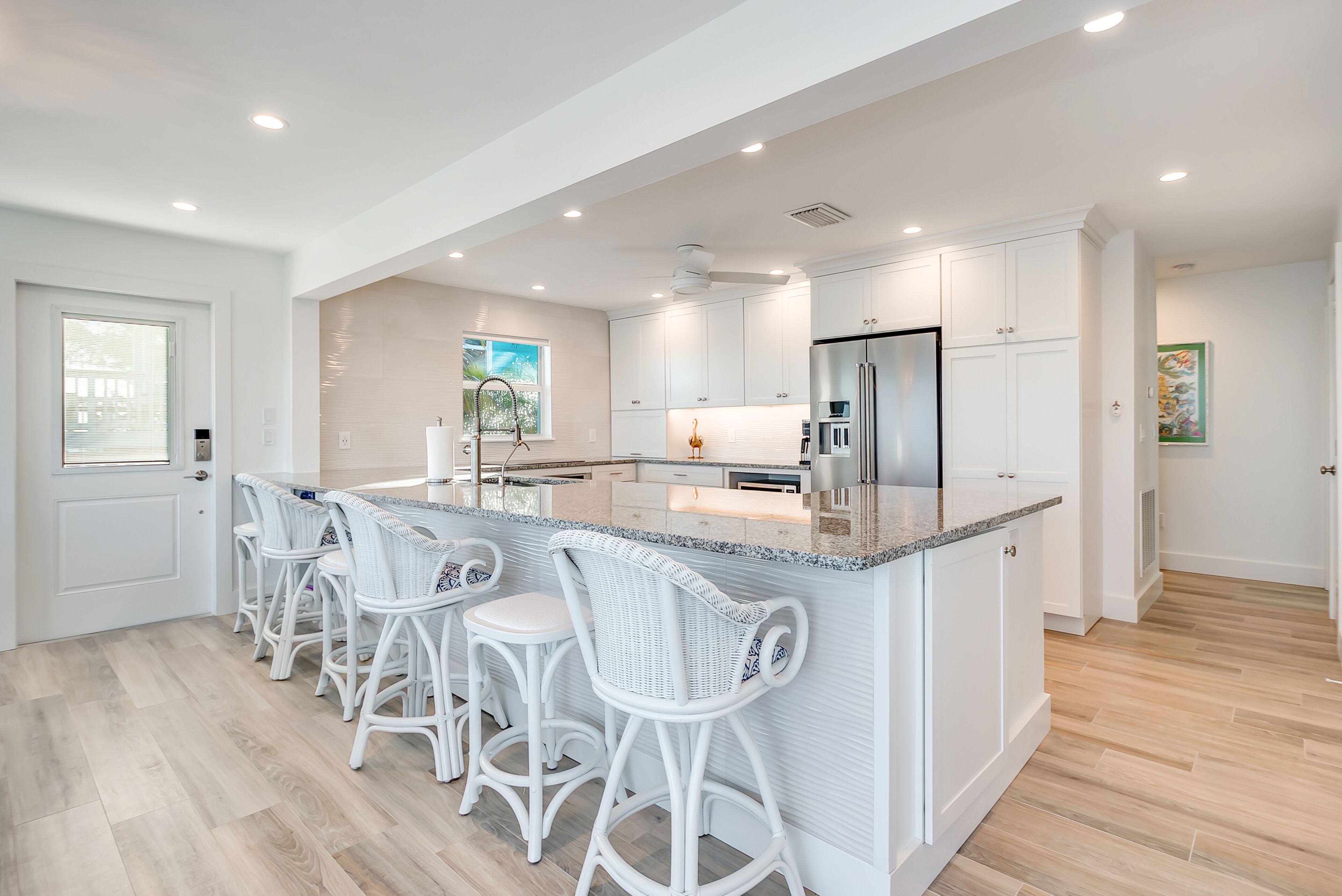 A modern kitchen with white cabinetry, a central island with bar stools, and a stainless steel refrigerator.