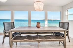 A dining area with a wooden table and chairs, a woven bench, and a chandelier. - Windows on the Water "W.O.W"  An ocean front oasis!   (Captiva)