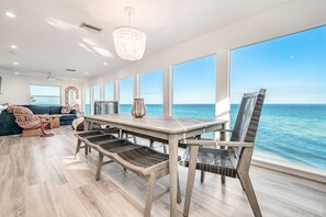Un'ampia stanza con un grande tavolo da pranzo, sedie in vimini e vista sull'oceano.